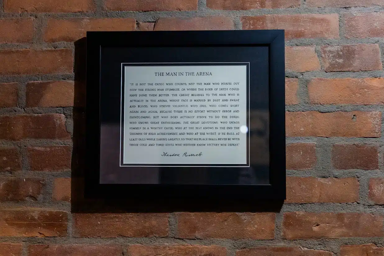 The Man in the Arena quote by Theodore Roosevelt, framed on brick wall